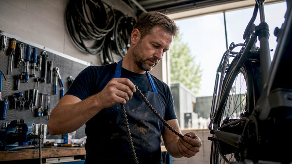 Een fietsenmaker bekijkt in zijn werkplaats nauwkeurig de versleten ketting van een e-bike.